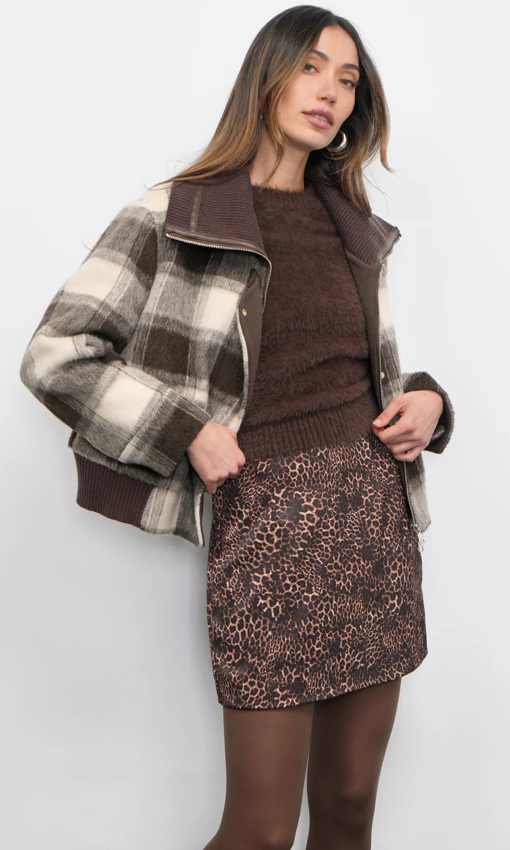 Woman wearing a plaid jacket, brown sweater, and leopard print skirt on a white background
