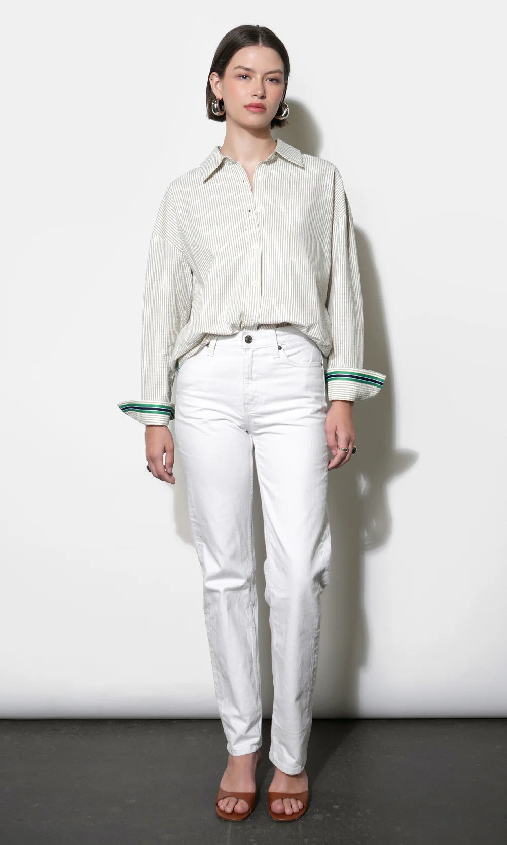 Woman wearing a light-colored blouse and white pants against a plain background