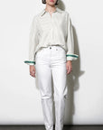 Woman wearing a light-colored blouse and white pants against a plain background