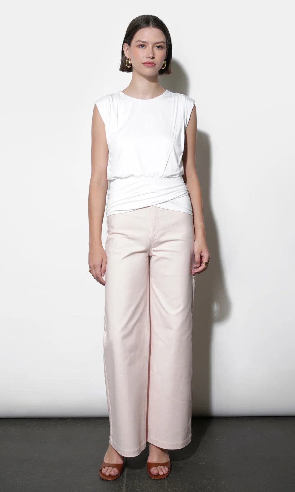 Woman wearing a white sleeveless top and light pink pants against a white background