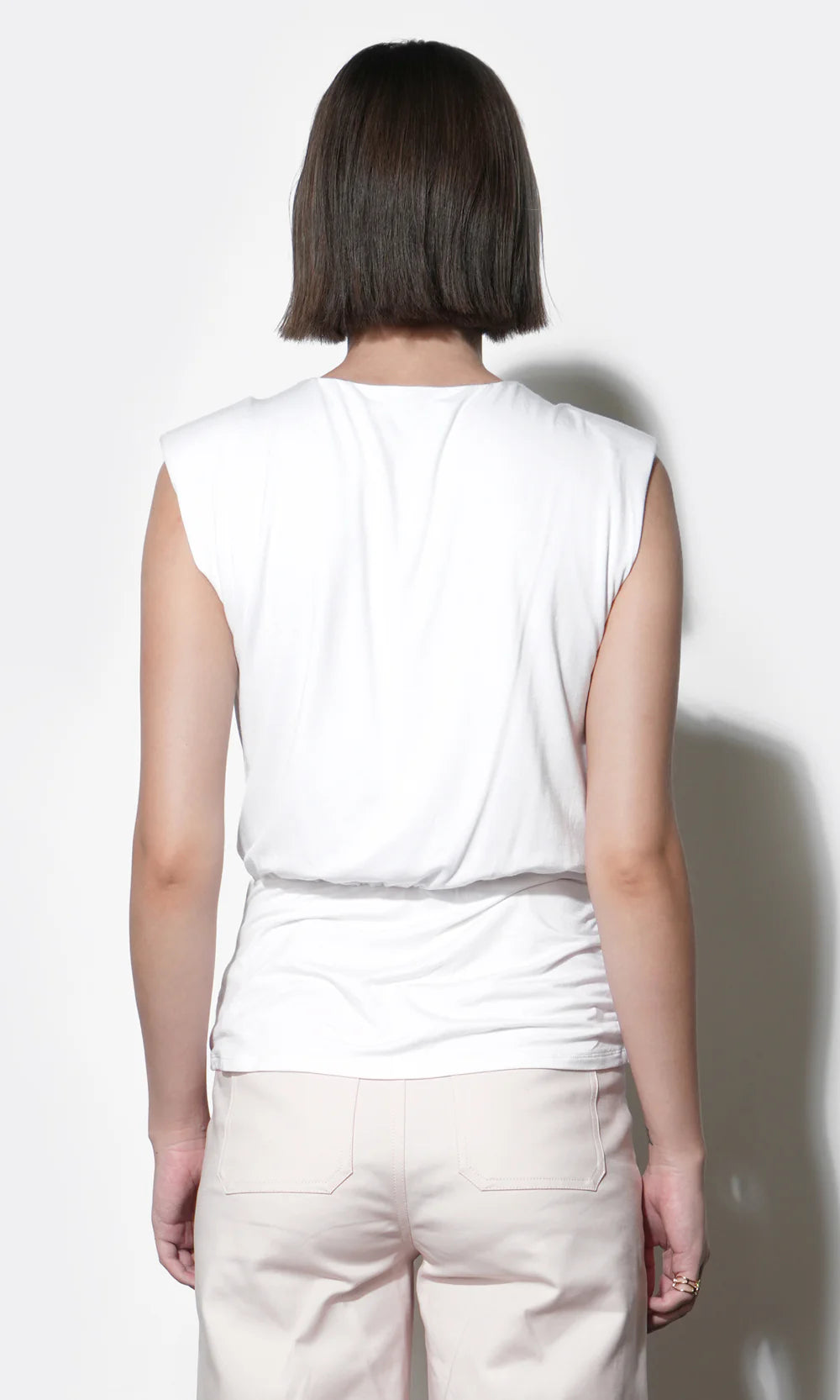 Person wearing a white sleeveless top and beige pants against a white background