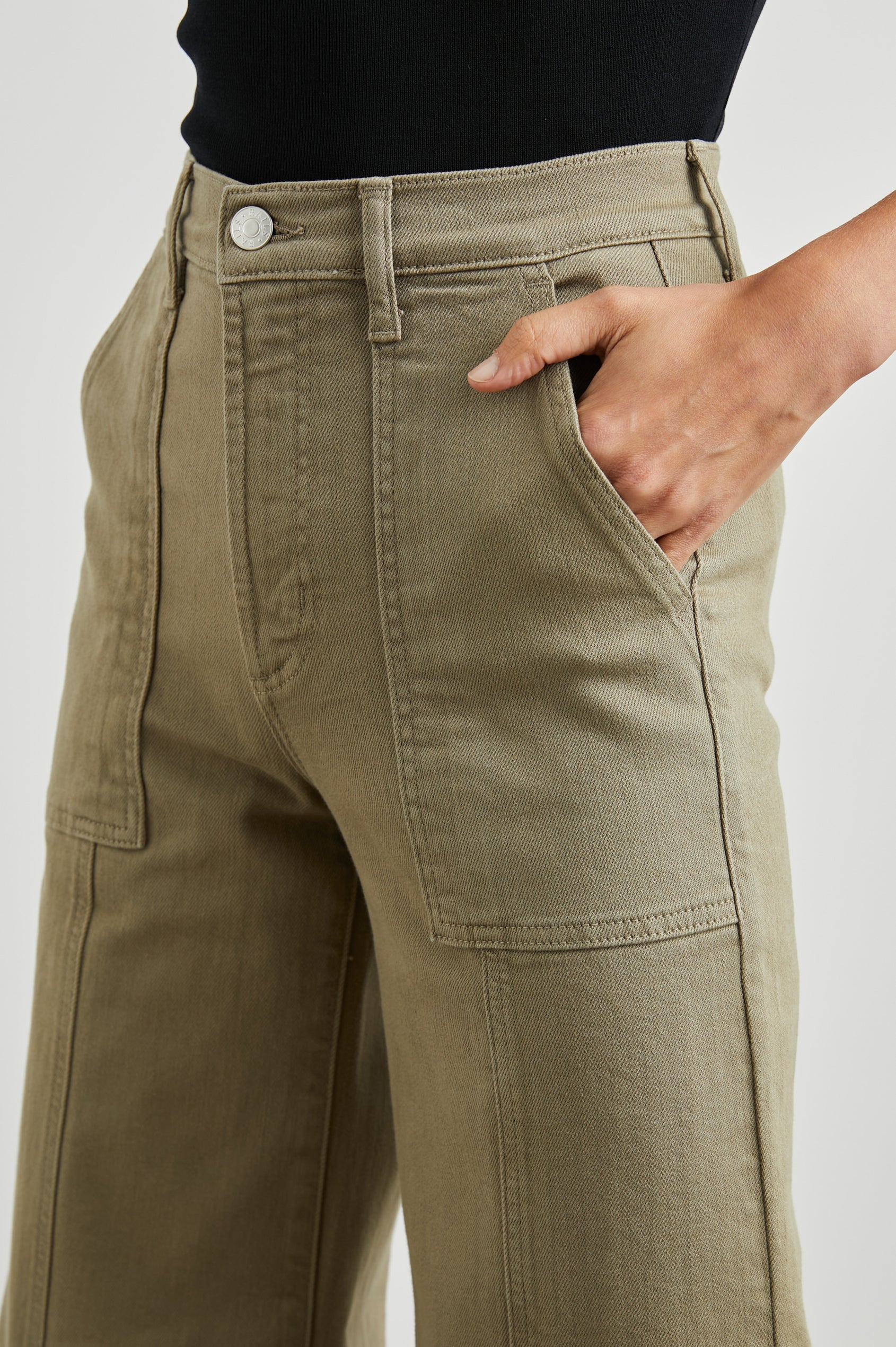 Person wearing olive green pants with a plain background