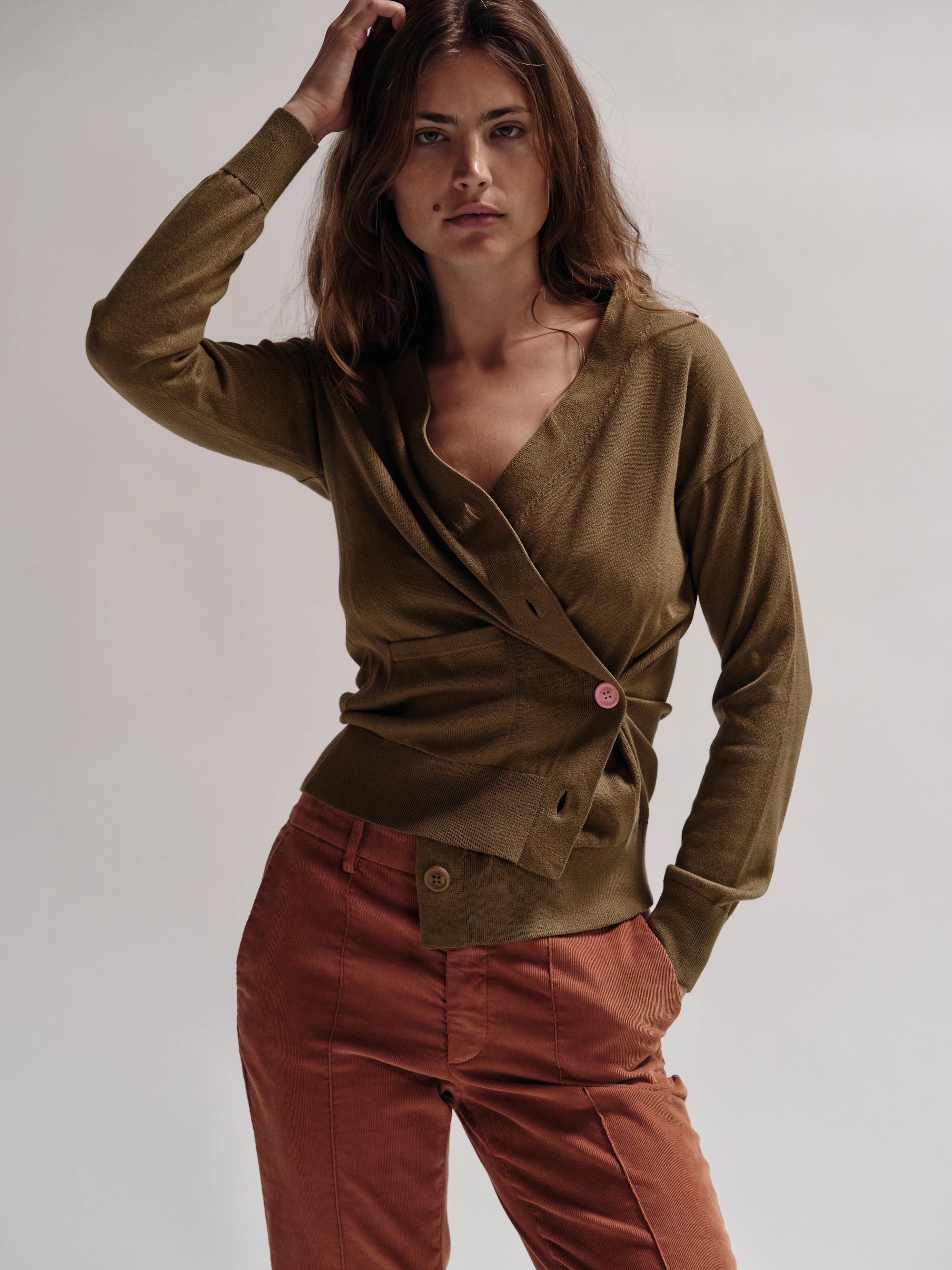Woman wearing a green cardigan and red pants against a plain background