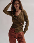 Woman wearing a green cardigan and red pants against a plain background