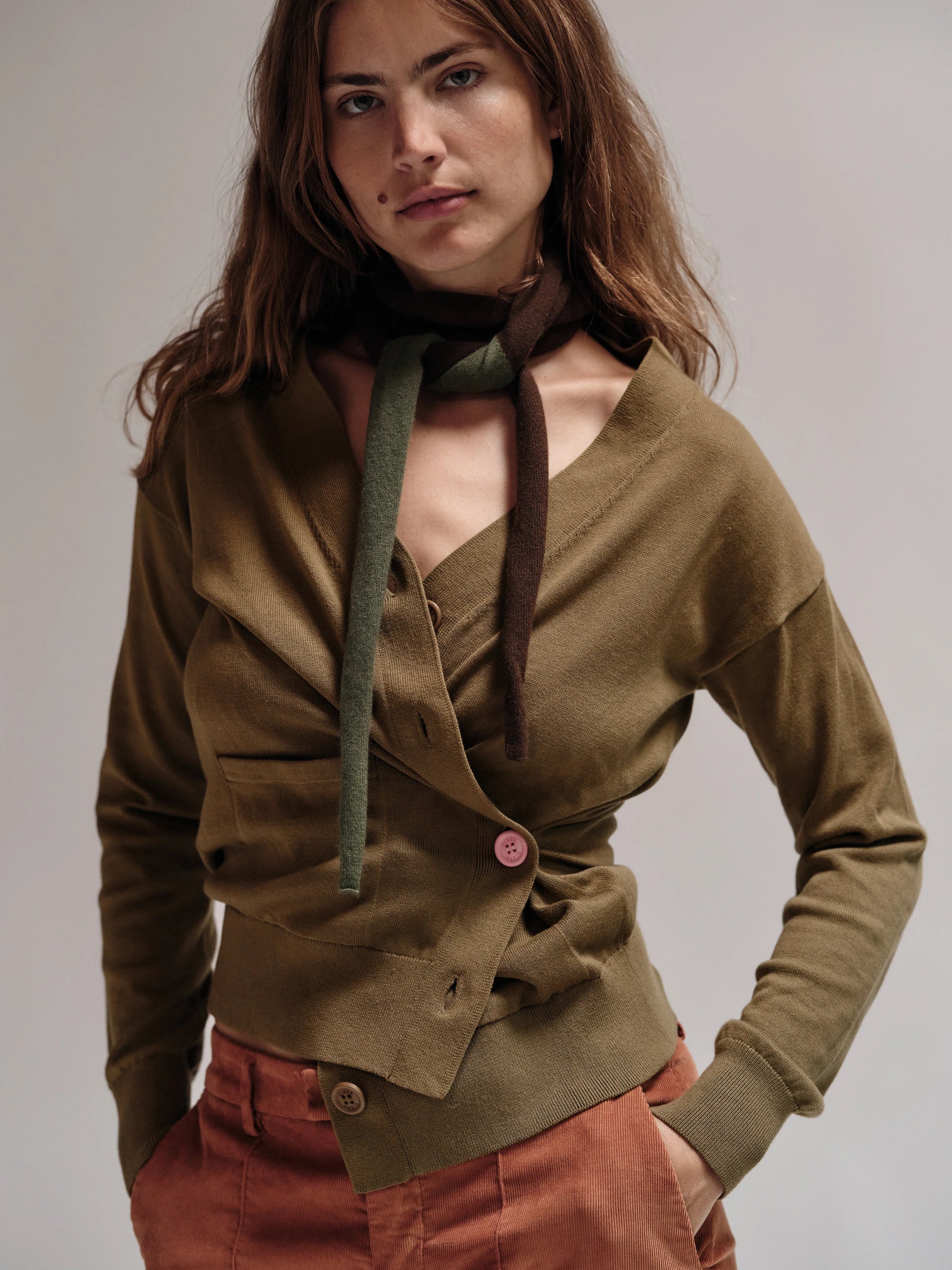 Woman wearing a green cardigan over a brown top with a scarf, on a plain background
