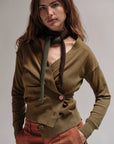 Woman wearing a green cardigan over a brown top with a scarf, on a plain background