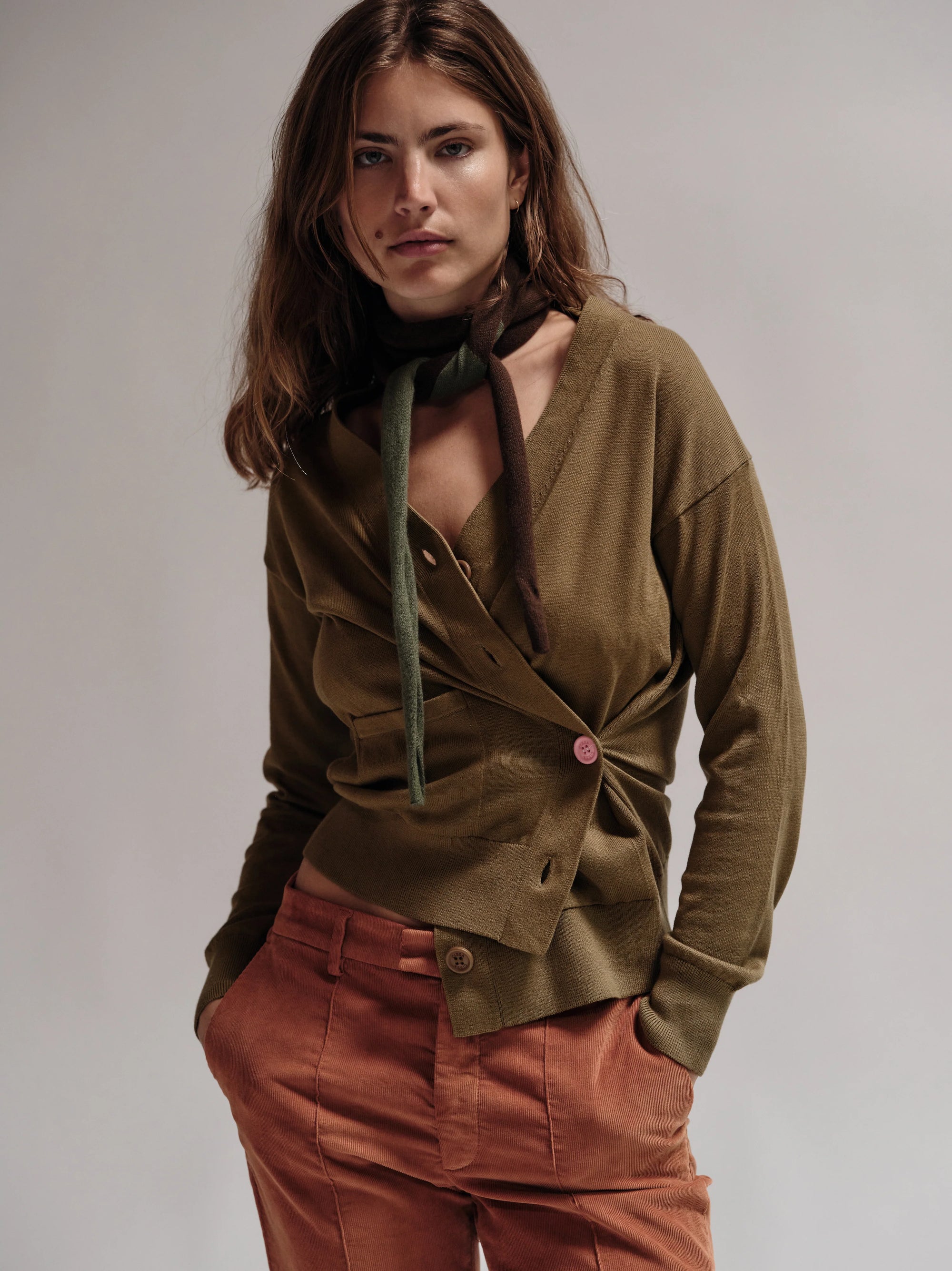 Woman wearing a green cardigan and pink pants against a plain background