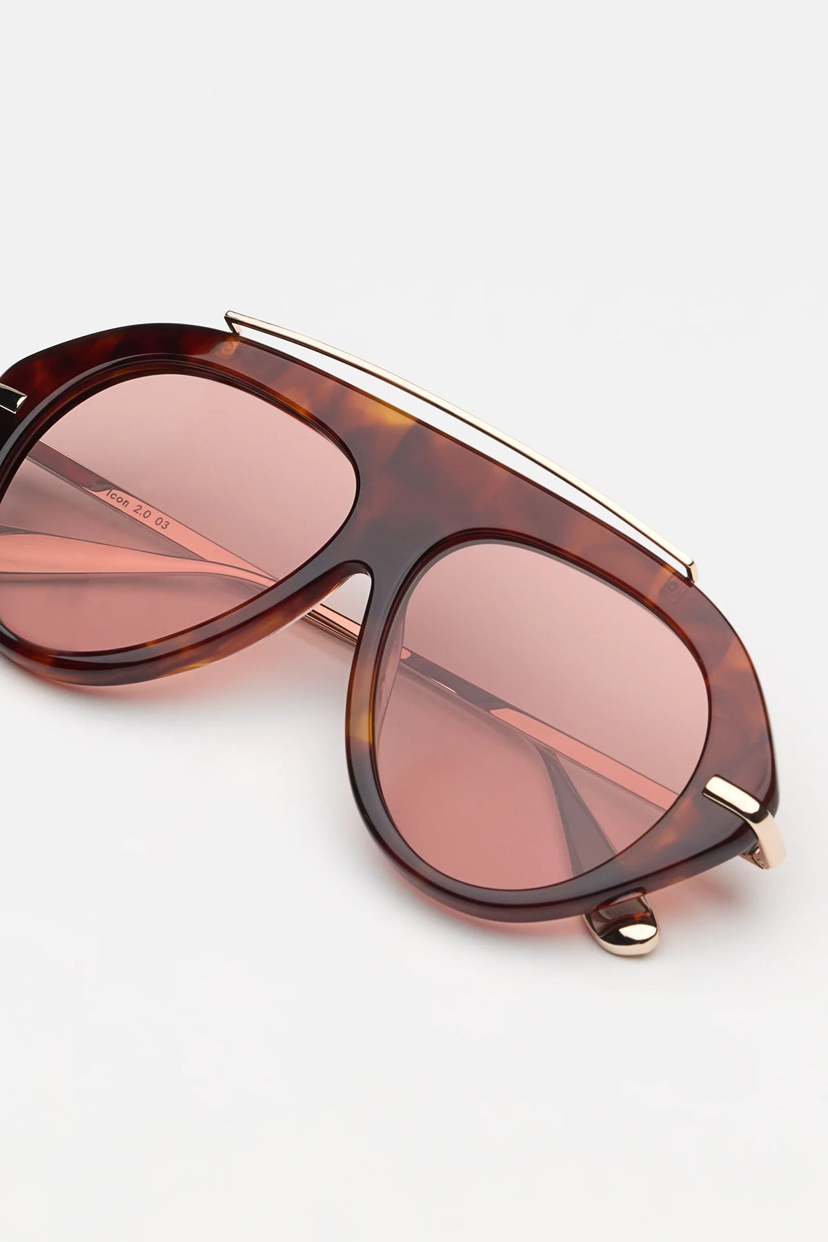 tortoise sunglasses with gold accents and light red lenses on a grey background 