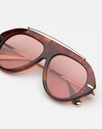 tortoise sunglasses with gold accents and light red lenses on a grey background 