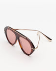 tortoise sunglasses with gold accents and light red lenses on a grey background 