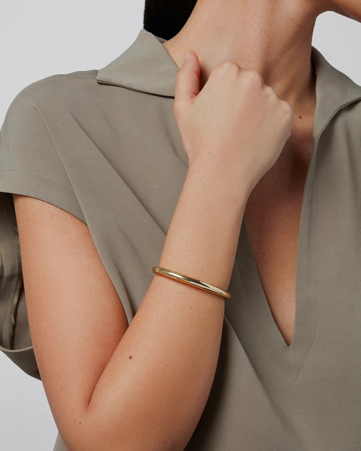 Person wearing a gold bracelet on a plain background