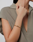 Person wearing a gold bracelet on a plain background