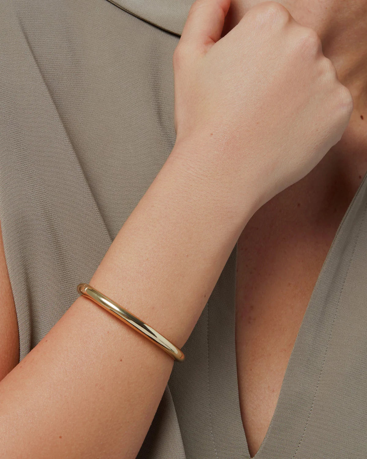 Gold bracelet on a wrist with a neutral background