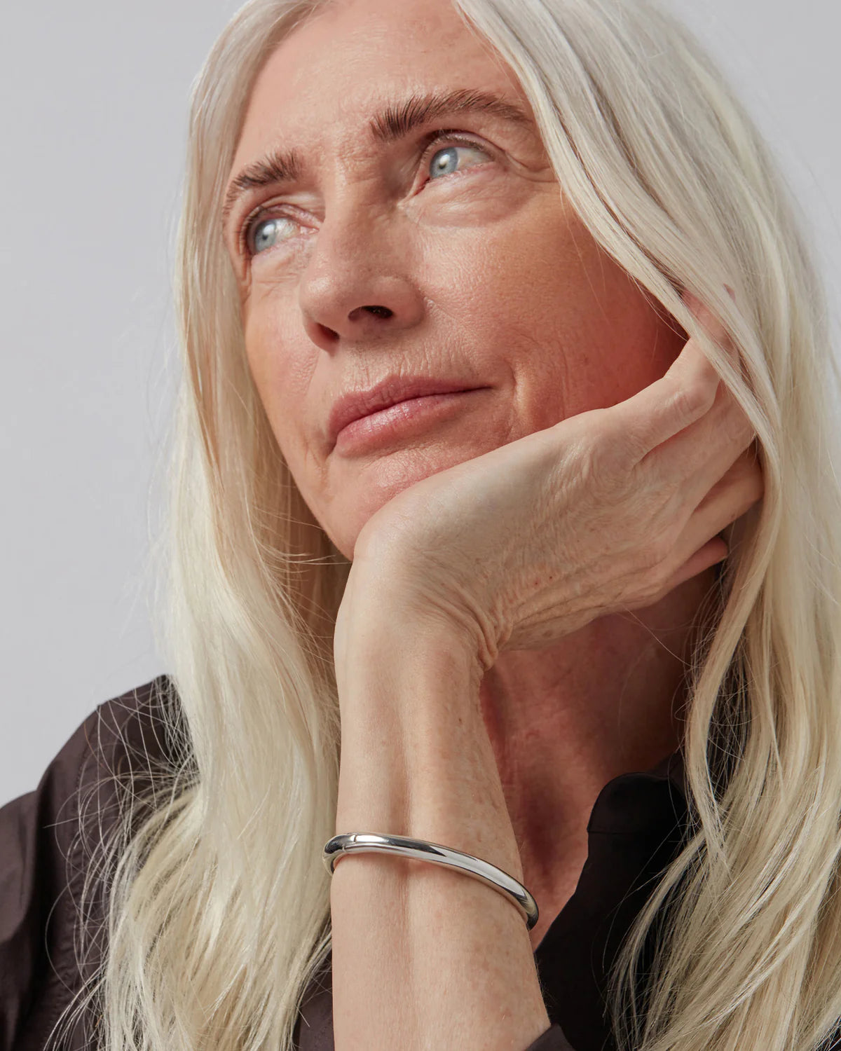 Woman with long blonde hair and a silver bracelet on a plain background