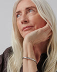 Woman with long blonde hair and a silver bracelet on a plain background