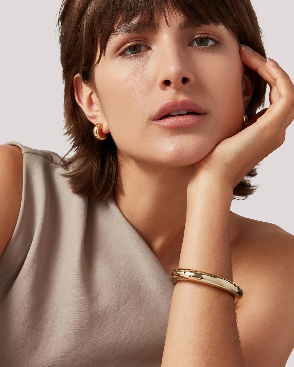 Woman wearing gold earrings and bracelet against a neutral background