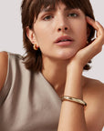 Woman wearing gold earrings and bracelet against a neutral background