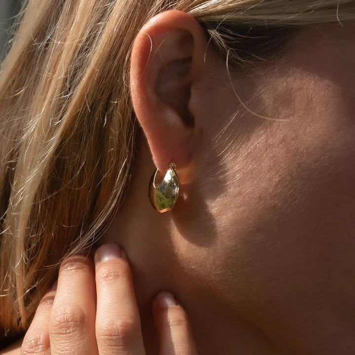 Close-up of a person wearing a gold earring with a hand adjusting it.