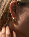 Close-up of a person wearing a gold earring with a hand adjusting it.