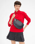 A model wearing a red long-sleeve button-up shirt and a dark gray pleated mini skirt, carrying a dark navy woven leather fanny pack across their waist