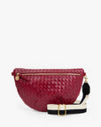A woven leather fanny pack in deep burgundy red, featuring a gold-tone zipper, a black and white striped webbed shoulder strap with a gold buckle, and a small gold charm.