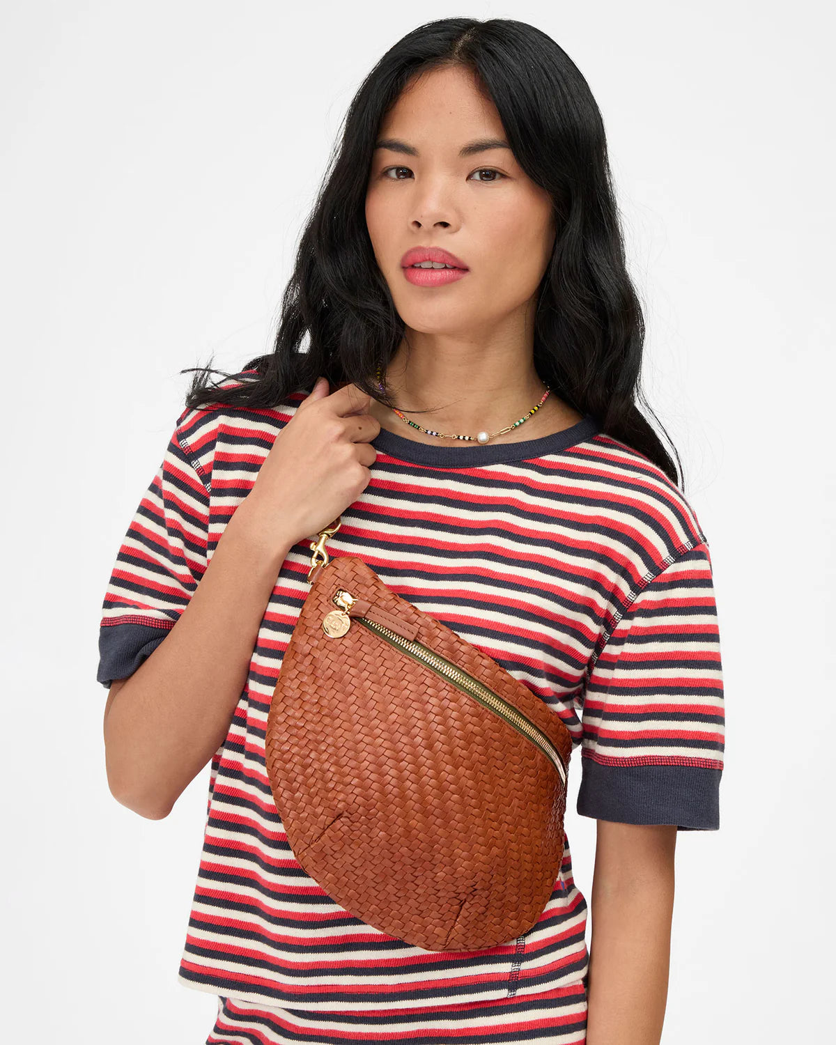 Woman wearing a striped shirt with a brown woven bag over her shoulder on a white background