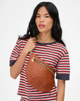 Woman wearing a striped shirt with a brown woven bag over her shoulder on a white background