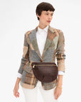 A model wearing a brown croc-embossed woven belt bag with a gold zipper, styled over a multicolor patchwork plaid blazer and white shirt.