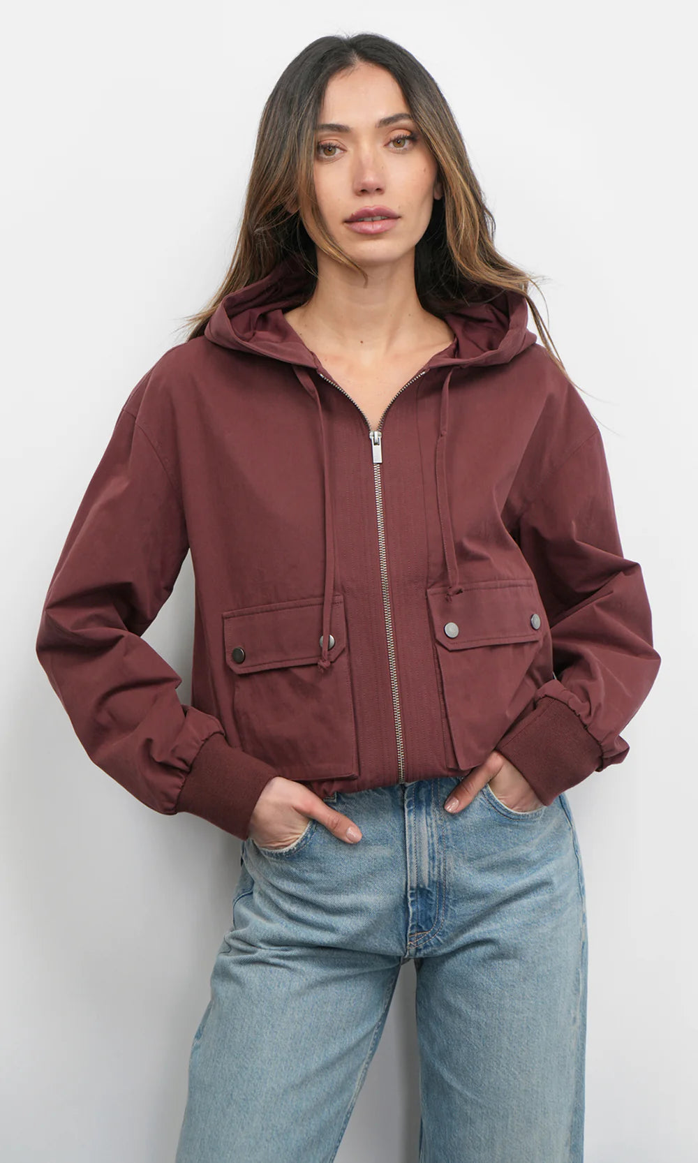 Woman wearing a maroon jacket and light blue jeans against a white background