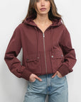 Woman wearing a maroon jacket and light blue jeans against a white background