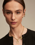 Woman wearing a gold necklace with a 'M' pendant against a neutral background