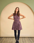 Woman wearing a patterned dress and dark tights standing against a plain background