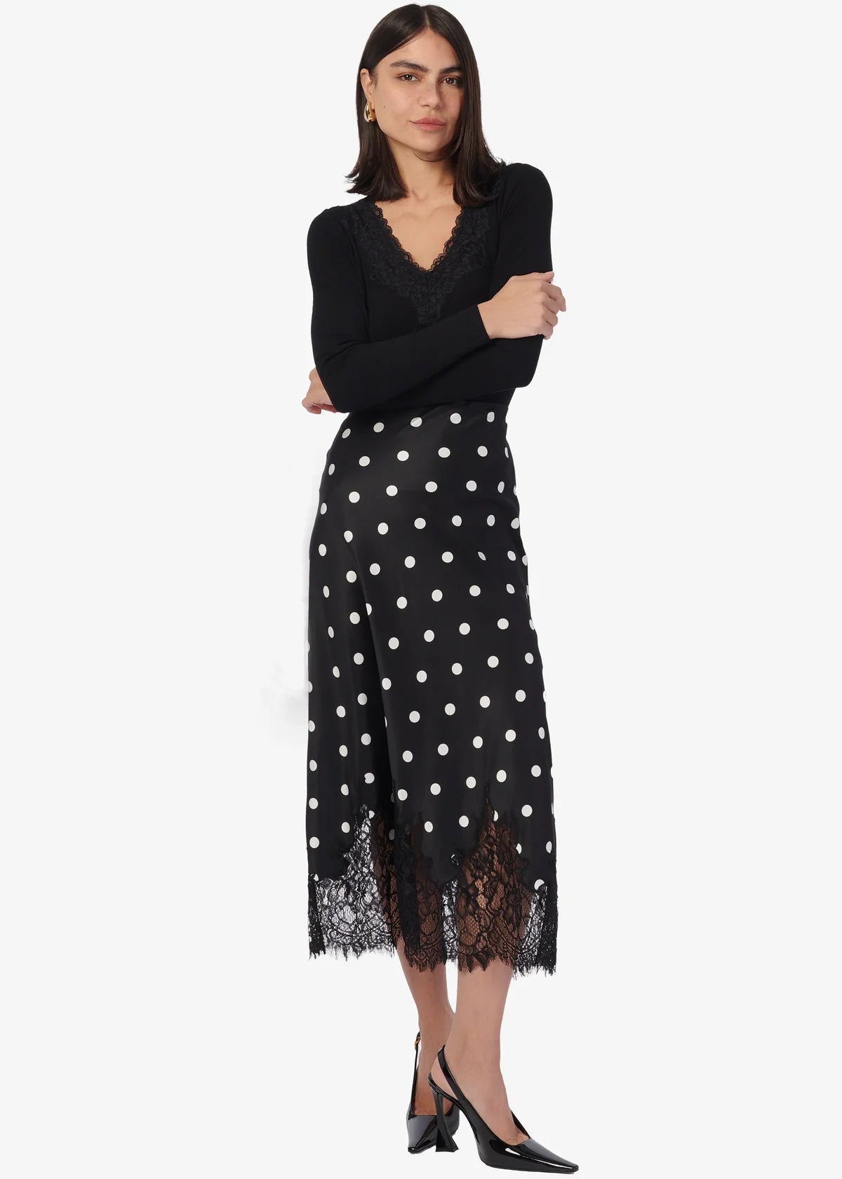 Woman wearing a black top and black polka dot skirt with lace trim on a white background