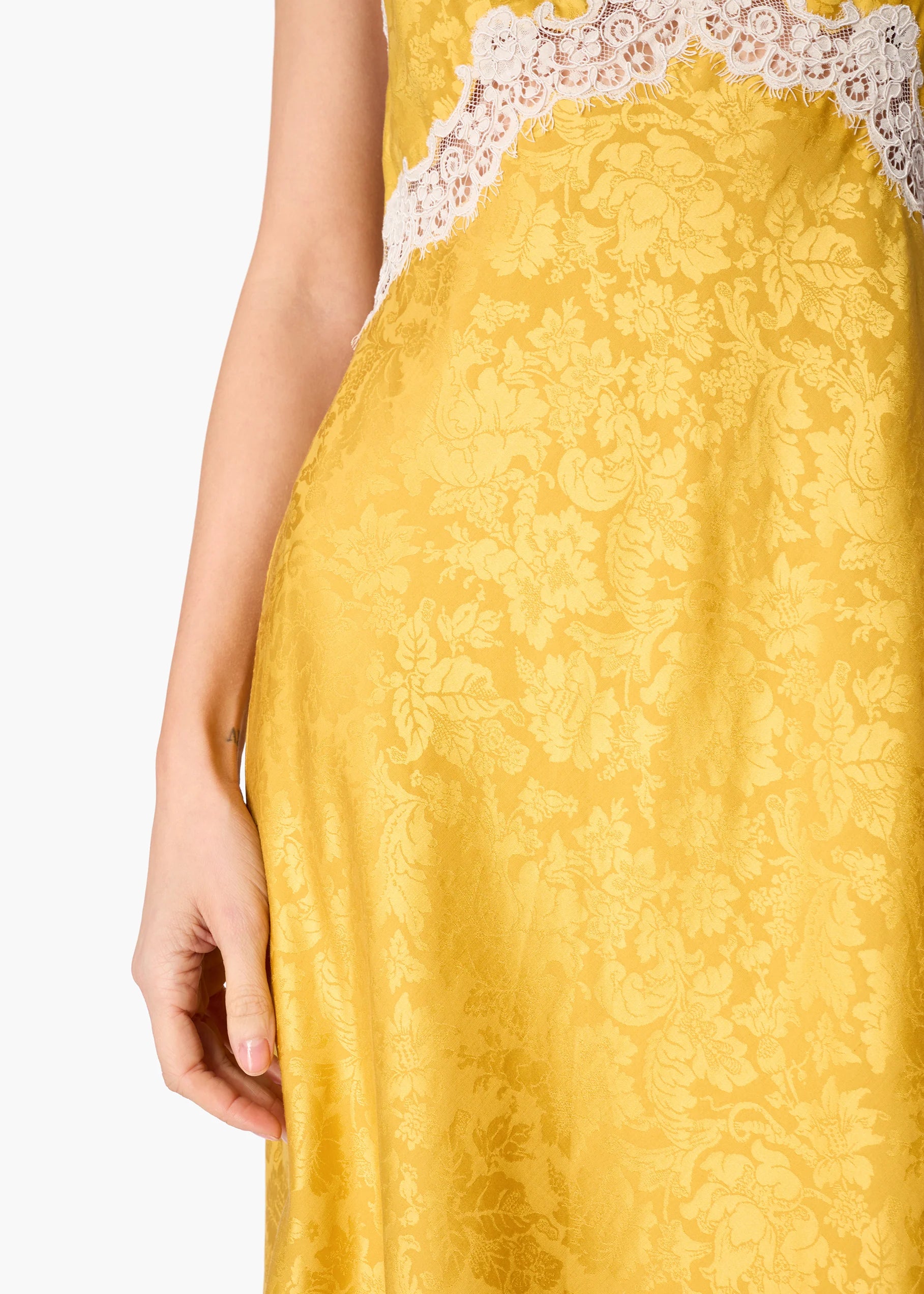 Close-up of a yellow jacquard dress with a white lace bodice trim, shown on a model against a white background.