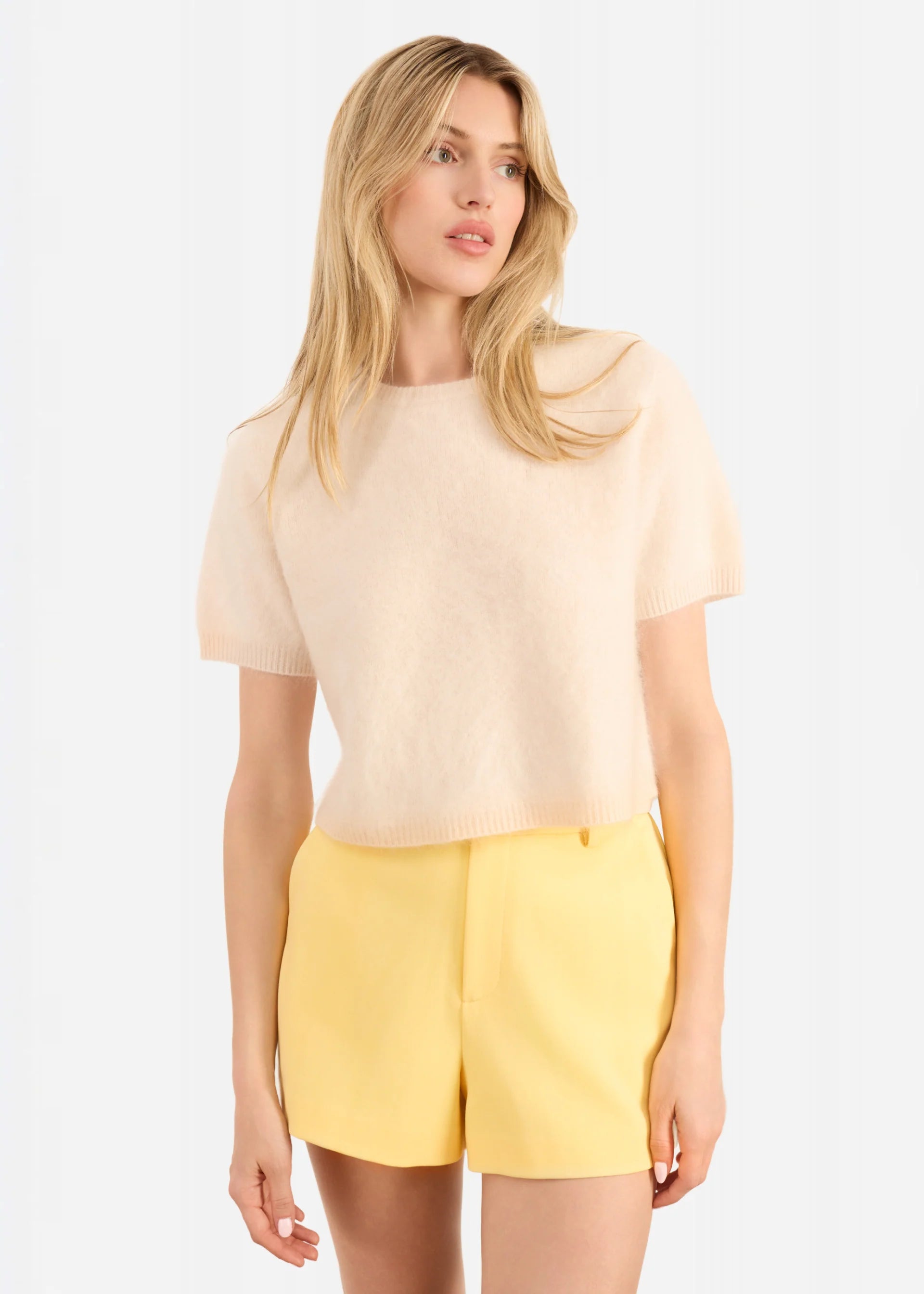 Woman wearing a beige top and yellow shorts on a white background