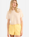 Woman wearing a beige top and yellow shorts on a white background