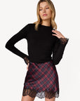 Woman wearing a black top and plaid skirt with lace details on a white background