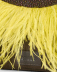 Close-up of a Staud handbag featuring bright yellow ostrich feather fringe over a dark brown suede body with a beaded waistband and a Staud leather logo patch.