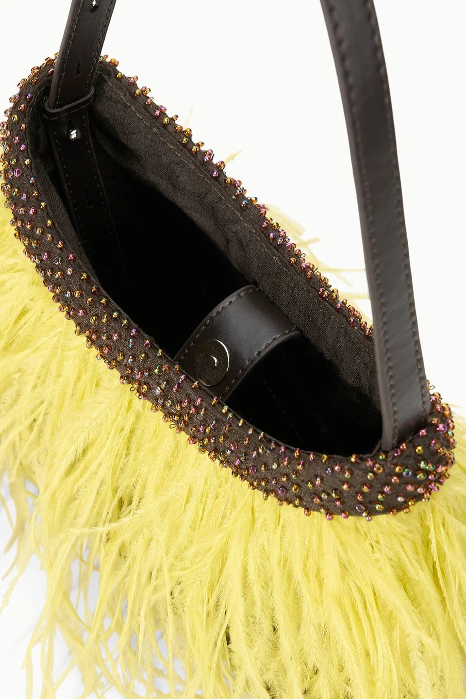 Close-up of a handbag with a bright yellow feathered exterior, a dark brown leather trim adorned with iridescent rhinestones, and a black interior.