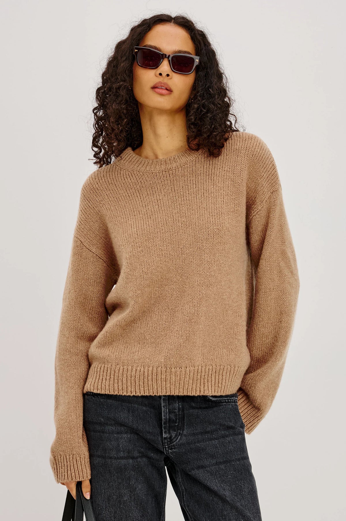 Woman wearing a brown sweater and sunglasses on a plain background