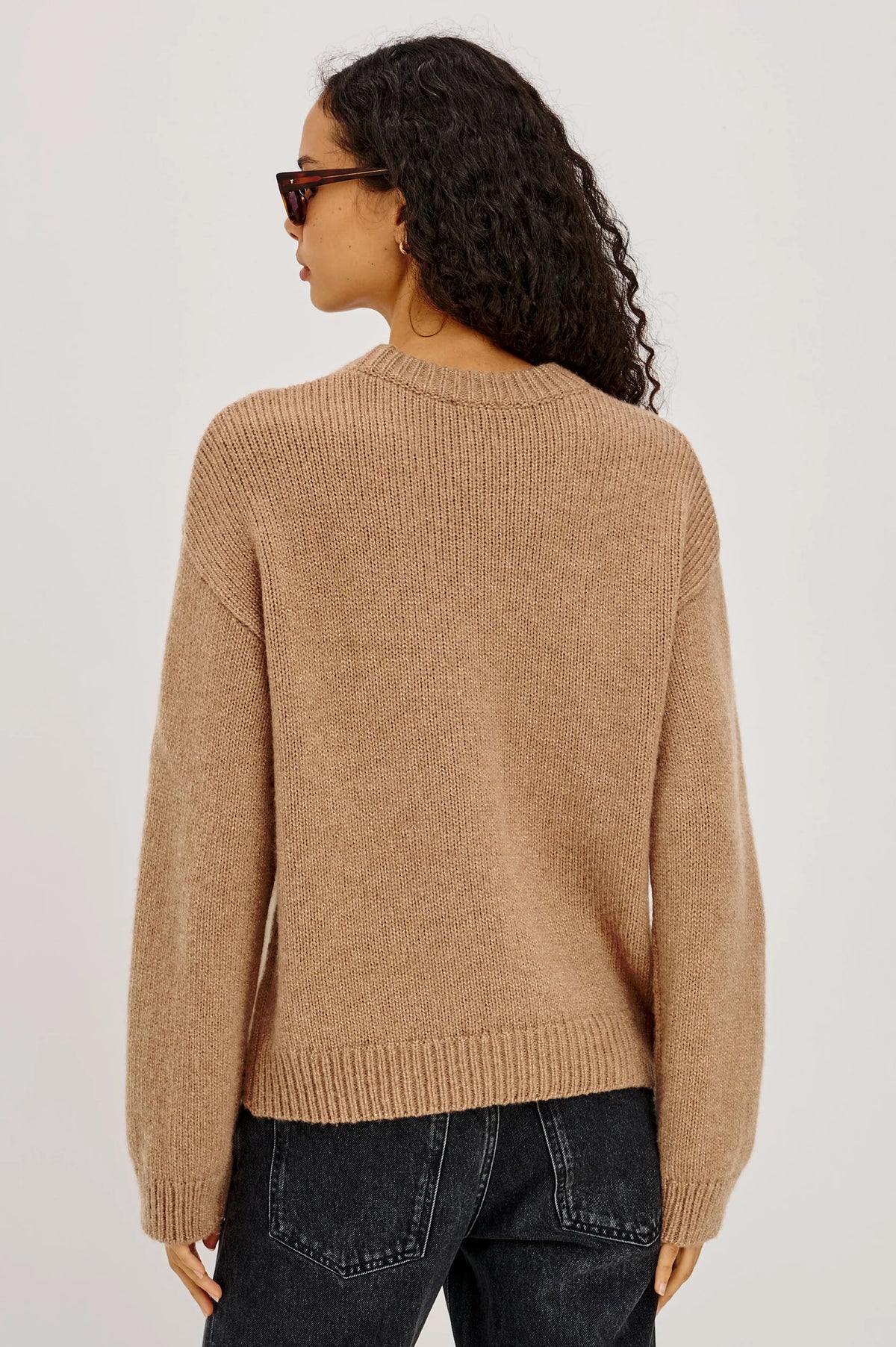 Person wearing a beige sweater and dark jeans on a plain background