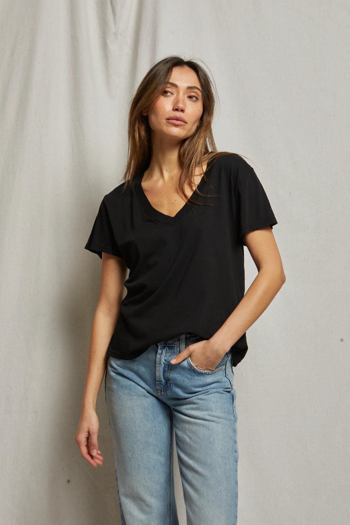 Woman wearing a black t-shirt and light blue jeans against a plain background, size S