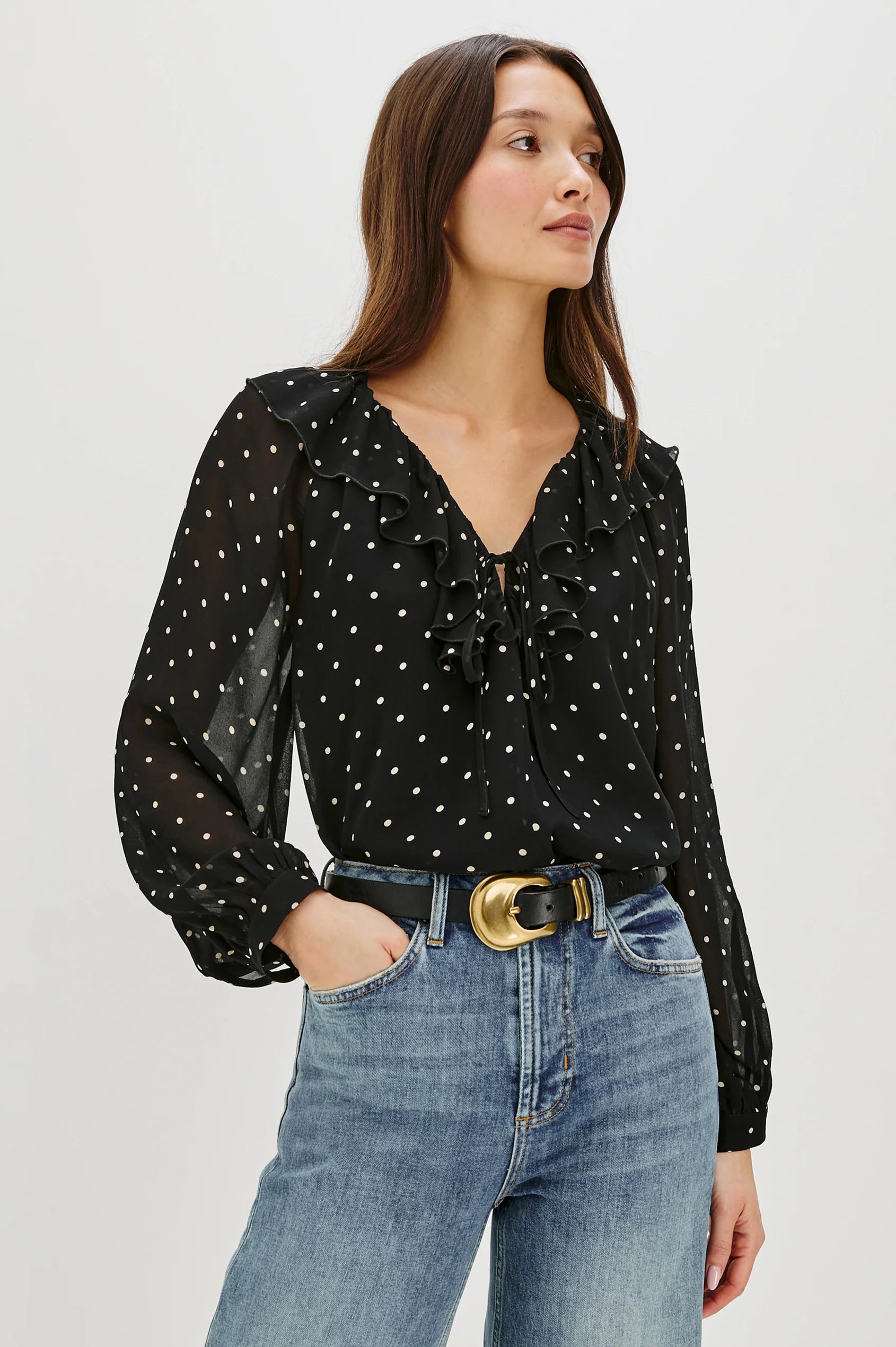 Woman wearing a black polka dot blouse and blue jeans on a white background
