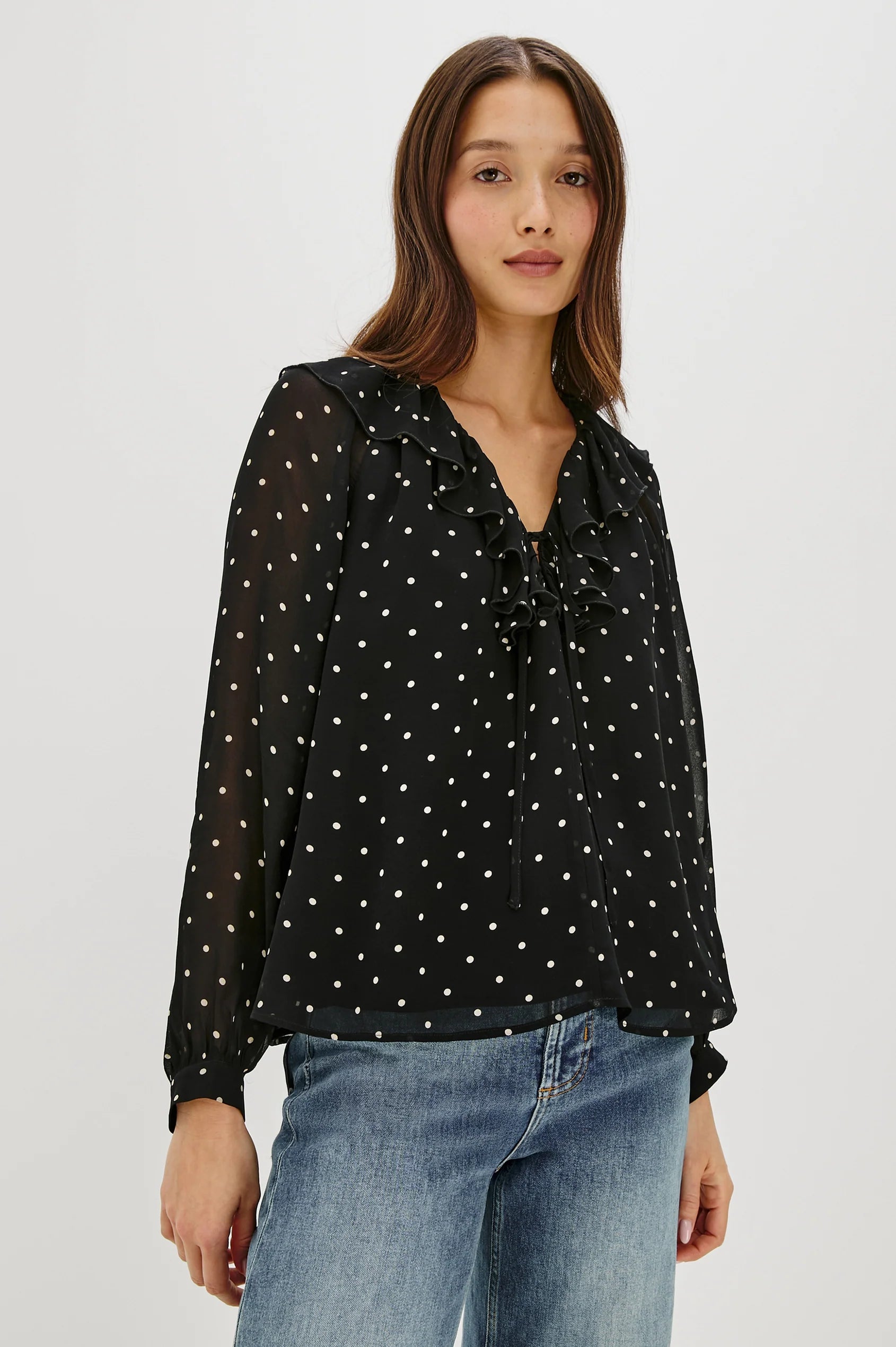 Woman wearing a black polka dot blouse and blue jeans on a white background