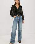 Woman wearing a black polka dot blouse and blue jeans on a white background