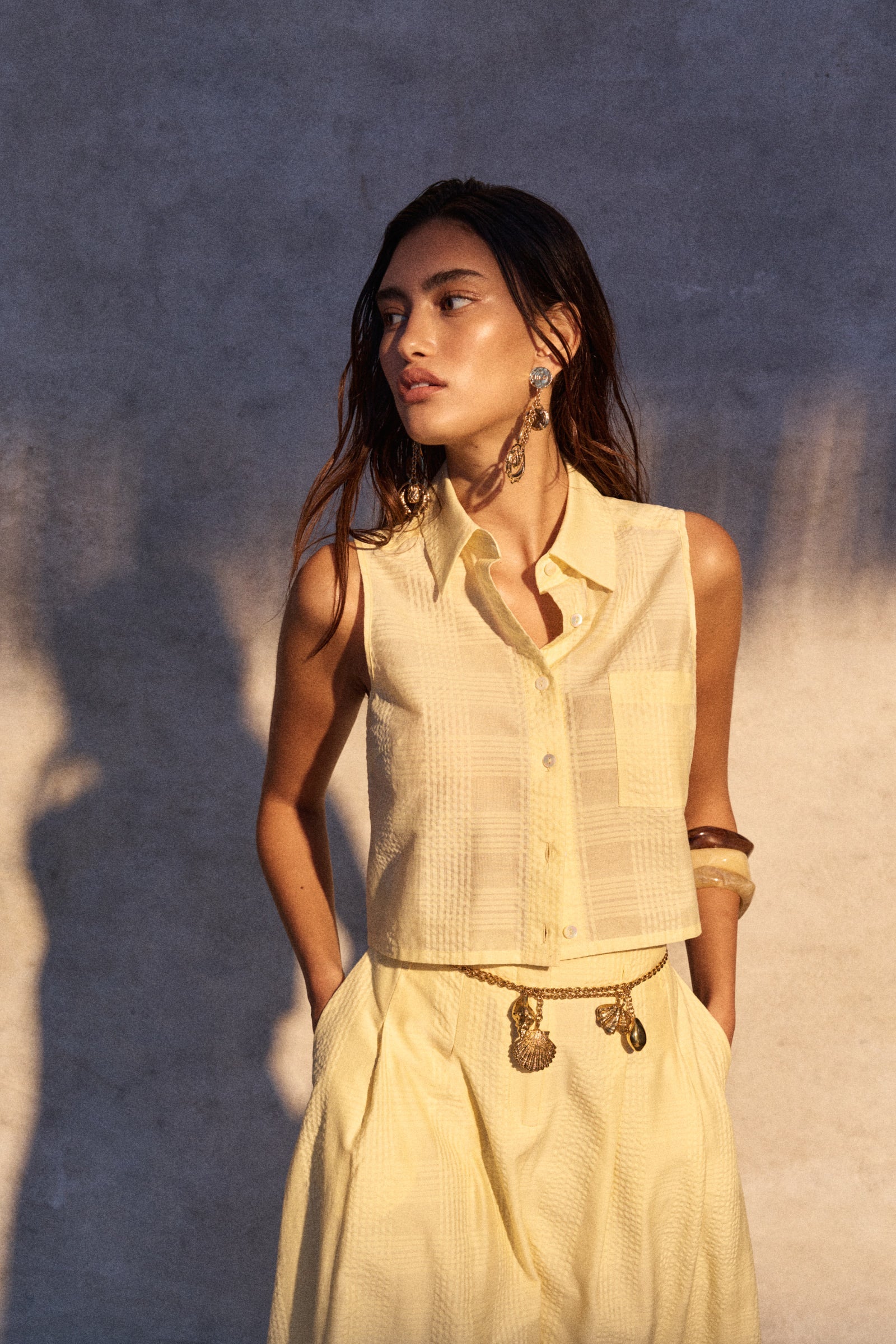 Woman wearing a light-colored sleeveless top and skirt against a textured wall.