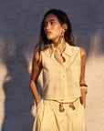 Woman wearing a light-colored sleeveless top and skirt against a textured wall.