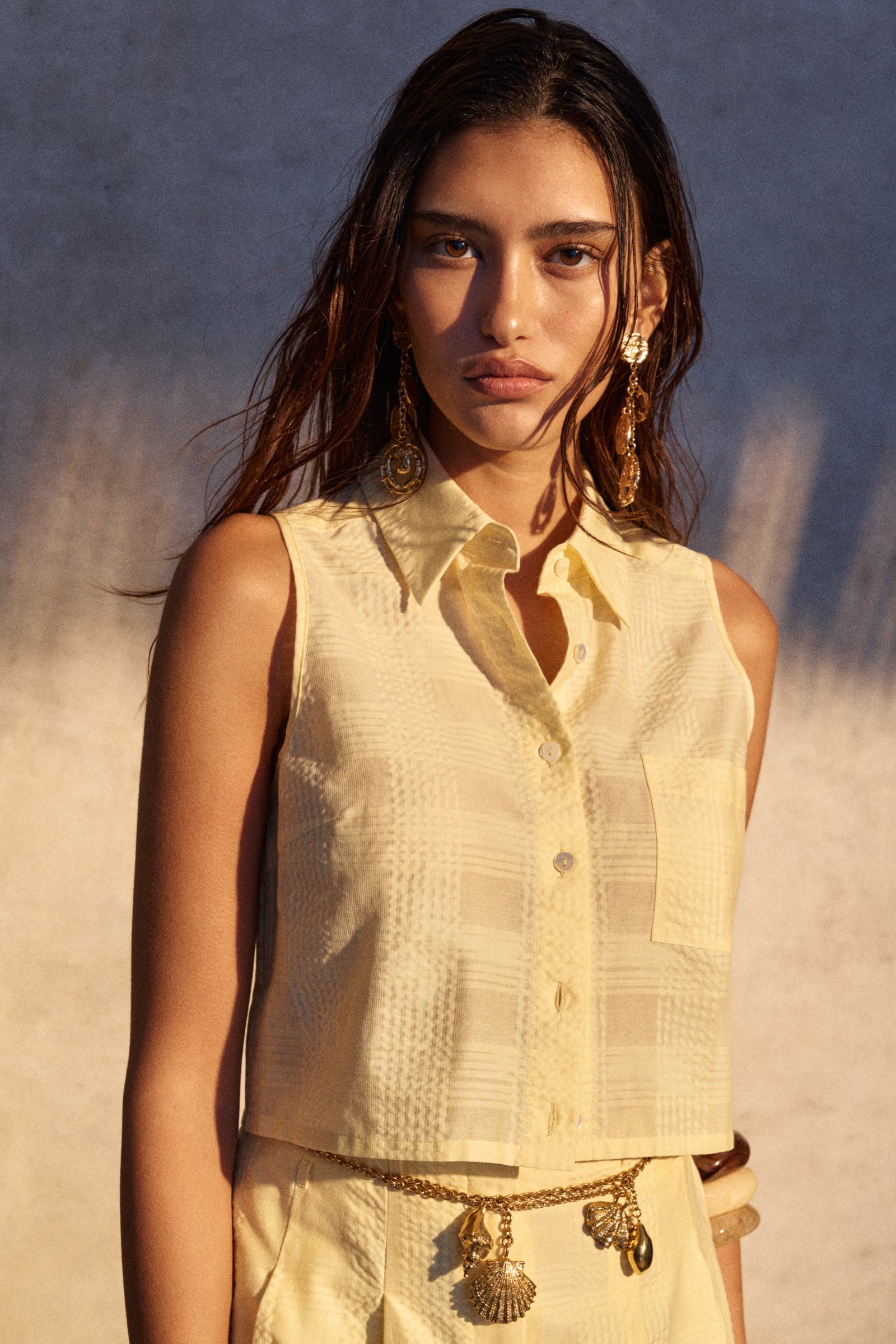 Woman wearing a light-colored sleeveless top with a textured pattern against a neutral background