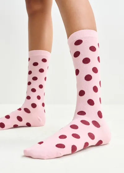 Pink socks with red polka dots worn by a person on a light gray background