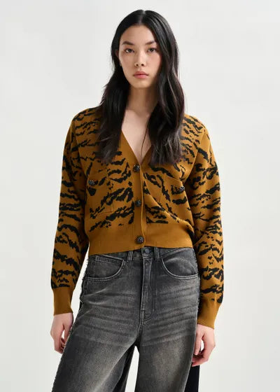 Woman wearing a mustard yellow cardigan with black tiger stripe pattern and gray jeans on a white background